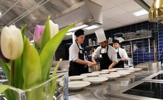 Students filling lunch plates in a professional kitchen.